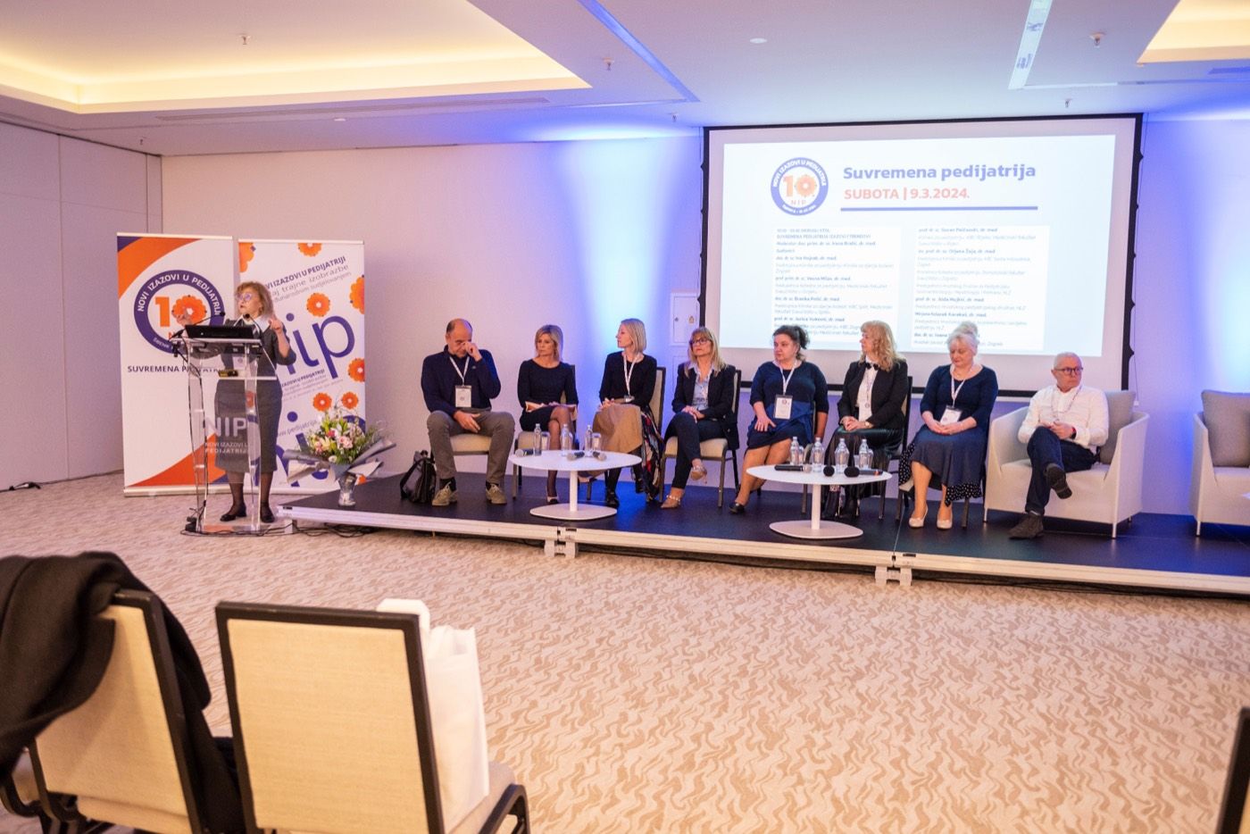 Panel na NiPP skupu — moderatorica za govornicom i osam panelista na pozornici